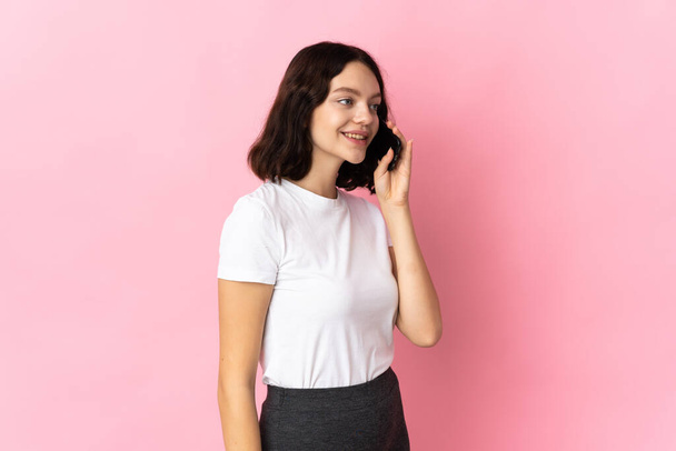 Teenager Ukrainian girl isolated on pink background keeping a conversation with the mobile phone - Foto, Imagem