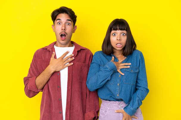 Young mixed race couple isolated on yellow background with surprise and shocked facial expression - Photo, Image