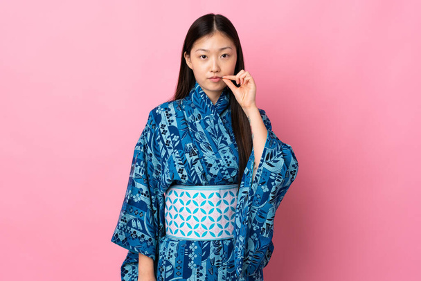 Young Chinese girl wearing kimono over isolated background showing a sign of silence gesture - Fotó, kép