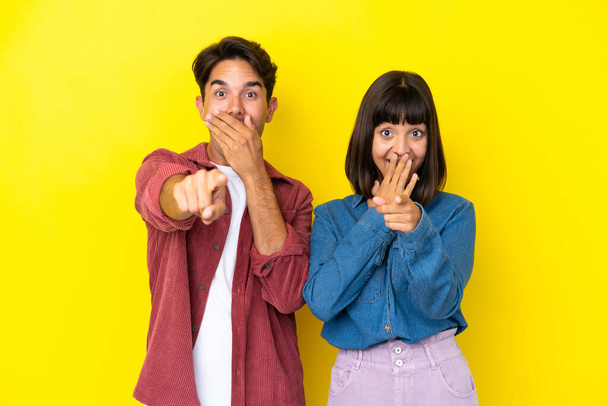 Nuori sekarotuinen pari eristetty keltaisella taustalla osoittaa sormella jotakuta ja nauraa - Valokuva, kuva