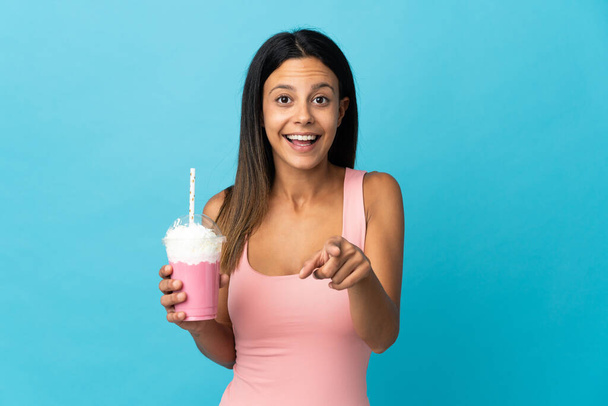 Young woman with strawberry milkshake surprised and pointing front - Foto, Imagem