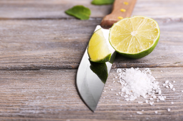 Still life with fresh lime, knife and salt on old wooden table - Foto, imagen