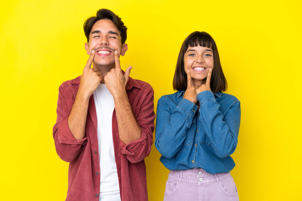 Молодая пара смешанной расы изолирована на желтом фоне улыбаясь со счастливым и приятным выражением - Фото, изображение