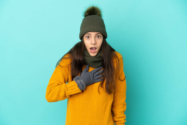 Nuori ranskalainen tyttö eristetty sinisellä taustalla talvella hattu yllättynyt ja järkyttynyt katsoessaan oikealle - Valokuva, kuva