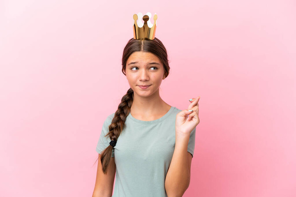 Little caucasian princess girl isolated on pink background with fingers crossing and wishing the best - Foto, Imagen