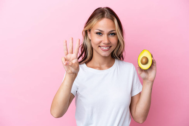 Young Russian woman holding avocado isolated on pink background happy and counting three with fingers - Photo, Image