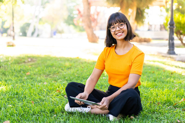 Junge brünette Frau im Freien mit einem Tablet mit glücklichem Gesichtsausdruck - Foto, Bild