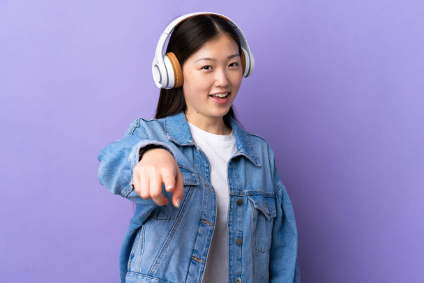 Young Chinese girl over isolated purple background listening music - 写真・画像