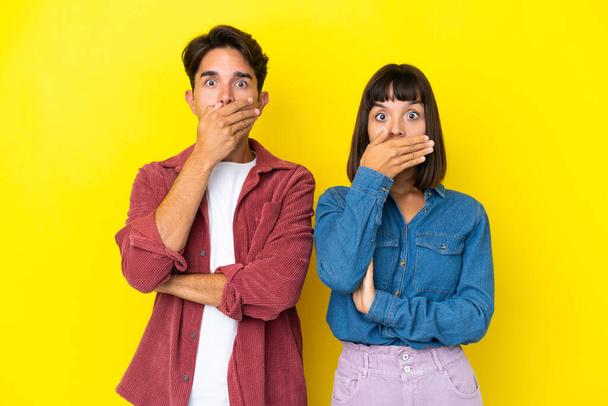 Jeune couple mixte isolé sur fond jaune couvrant la bouche avec les mains pour avoir dit quelque chose d'inapproprié - Photo, image