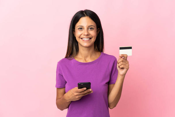 Кавказская девушка, изолированная на розовом фоне, покупает с мобильного с помощью кредитной карты - Фото, изображение