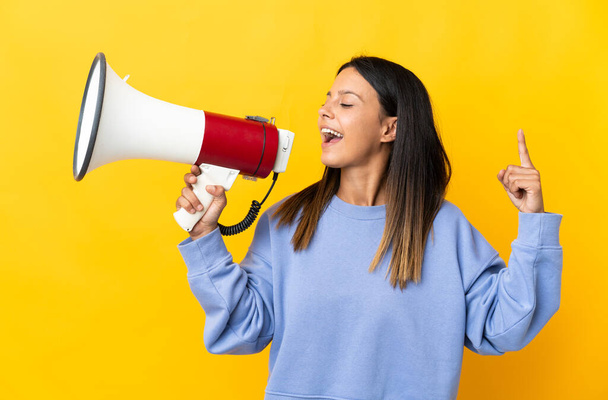 Caucasian girl isolated on yellow background shouting through a megaphone to announce something in lateral position - Foto, Bild