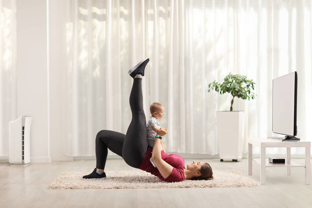 Mother exercising at home with her baby on her belly - Foto, Imagen
