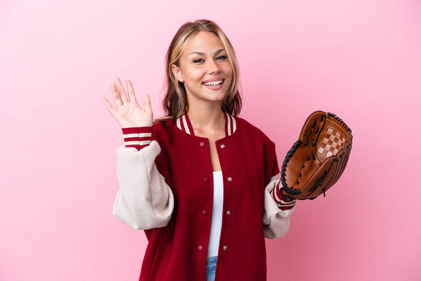Player Russian woman with baseball glove isolated on pink background saluting with hand with happy expression - Foto, imagen