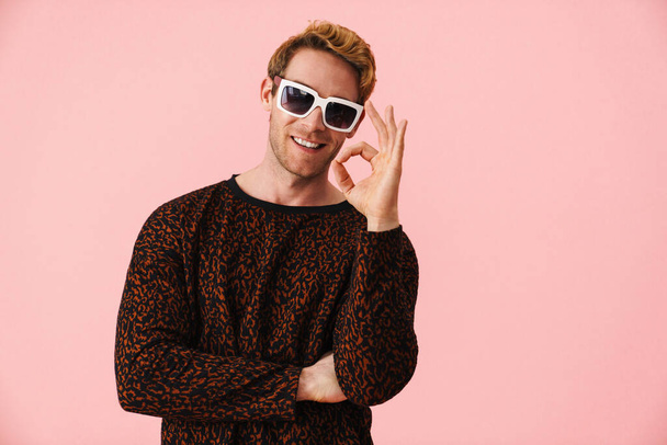 Happy mid aged blonde gay man in sunglasses standing over pink background showing ok - Foto, Bild