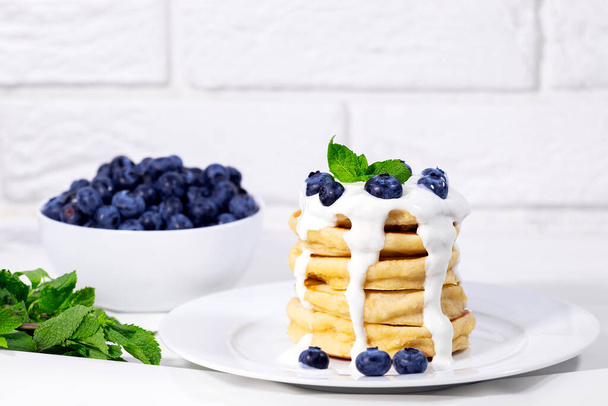 Блинчики с черникой с йогуртом и мятой на белом фоне, традиционный американский здоровый завтрак, копипространство, горизонтальное разрешение - Фото, изображение