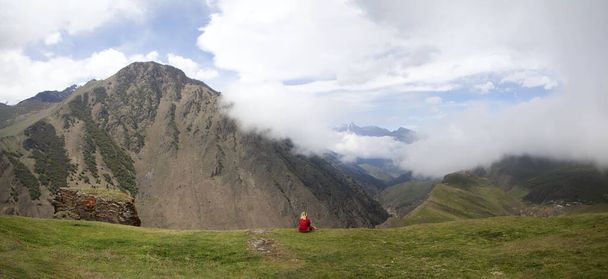Kırmızılı bir kadın bir uçurumda oturuyor, dağların arkasında. Digoria Dağı. Kuzey Osetya. - Rusya. 18 Mayıs 2021 - Fotoğraf, Görsel