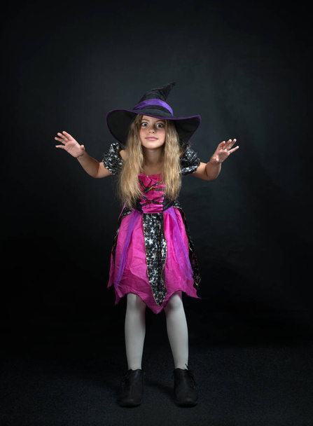 A girl dressed as a witch and a wide-brimmed hat for Halloween. - Zdjęcie, obraz