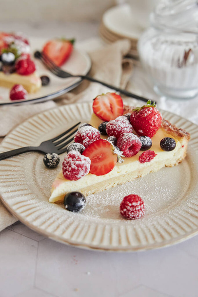 A selective focus shot of a piece of a delicious cheesecake on a plate with fresh berries on top - Foto, Imagem