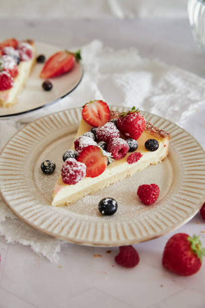 A selective focus shot of a slice of a delicious cheesecake on a plate with fresh berries on top - Foto, Bild