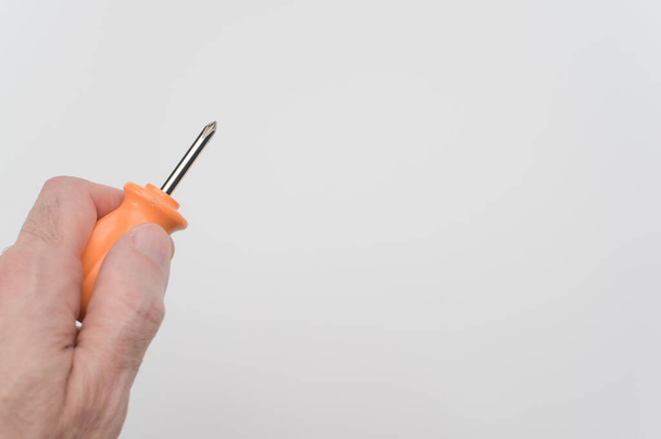 A hand of a male holding a small orange screwdriver on a white background - Foto, Imagem