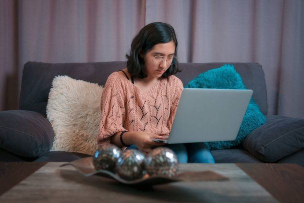Visão horizontal de um adolescente sentado no sofá com seu laptop, ela presta atenção à chamada de vídeo, tem aula virtual - Foto, Imagem