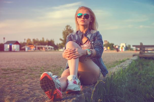 Hermosa moda joven mujer gafas de sol sentado y posando al atardecer Soleado al aire libre retrato
. - Foto, Imagen