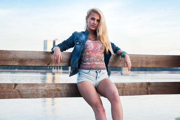 Draußen Porträt einer romantischen jungen Frau mit langen Beinen und Haaren in sommerlicher Freizeitkleidung, die auf einem Steg in der Nähe des Flusses steht. urbaner Lebensstil. Foto getönte warme Farben - Foto, Bild