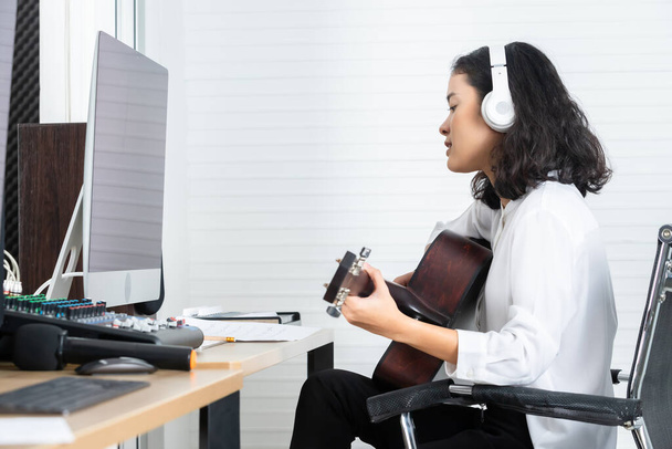 Professional musician young Asian woman vocalist Wearing Headphones plays guitar recording a song of the computer monitor of Software for recording and editing sounds in a professional studio - Foto, immagini