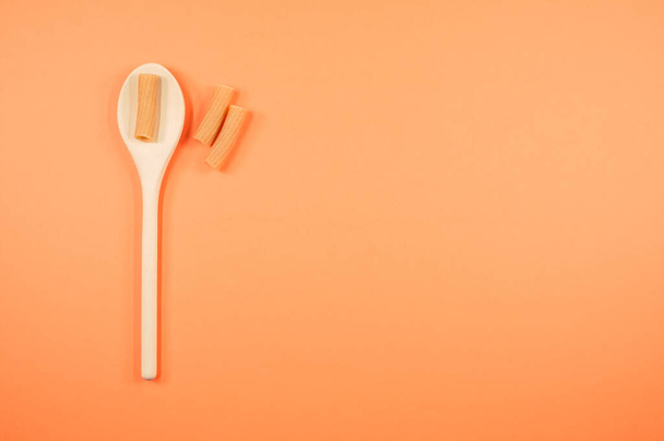 A top view shot of rigatoni on a spoon on an orange surface with free space for text - Photo, image