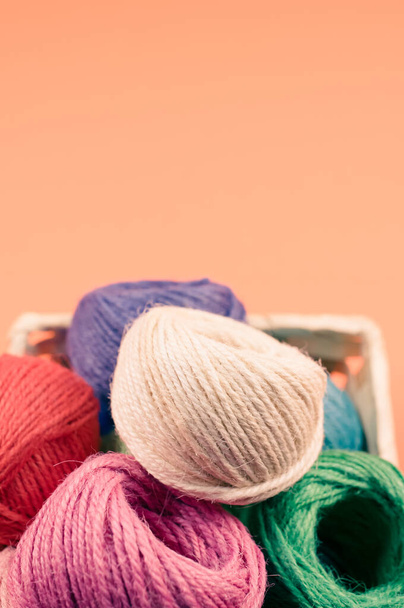 A vertical shot of a basket of colorful balls of yarn on an orange surface - Zdjęcie, obraz