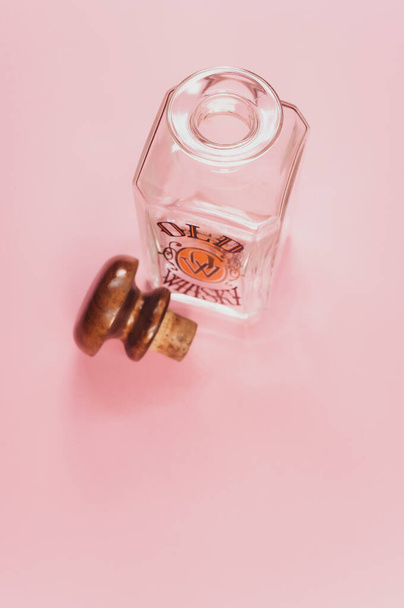 COMO, ITALY - Aug 13, 2021: A top view of an empty glass bottle for spirits drinks with a wooden cap isolated on a pink background - 写真・画像