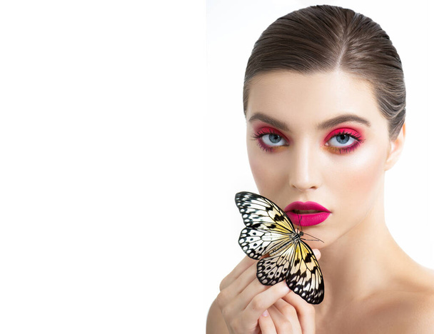 Beautiful young woman with perfect skin, long eyelashes and bright vivid pink make up posing with butterfly on her hand. Portrait of fashion beauty model with colorful professional makeup. SPA and wellness, make-up and skincare concept. - 写真・画像