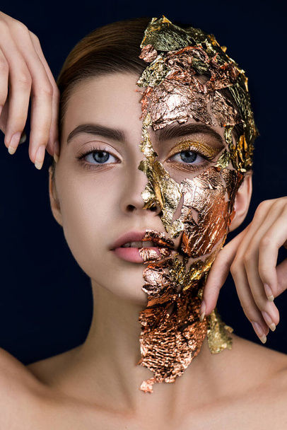 Beautiful young woman's face with golden makeup imitated luxury mask on half of her face and natural makeup on other half. SPA skin care and wellness concept. - Photo, image
