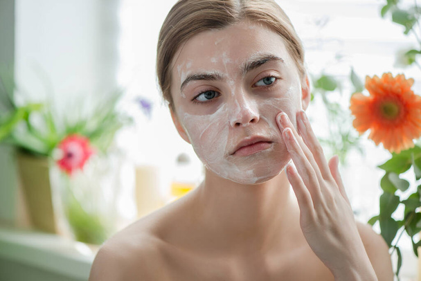 Beautiful young girl cleansing face with cosmetic facial skincare foam, gel or soap. Woman hame SPA procedures. - Fotó, kép