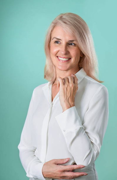 Attractive elderly woman with gray hair in casual clothes posing on a green background in the studio. Makeup and senior elderly skin care. Business woman smiling. - Foto, Imagen