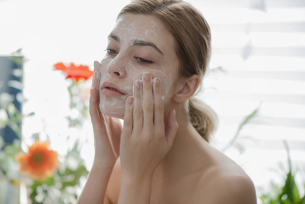 Beautiful young girl cleansing face with cosmetic facial skincare foam, gel or soap. Woman hame SPA procedures. - Fotografie, Obrázek