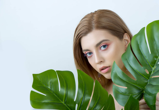 Beautiful young woman with perfect skin and natural make up posing front of plant tropical green leaves background. Teen model are of her face and body. SPA, wellness, bodycare and skincare. - Фото, изображение