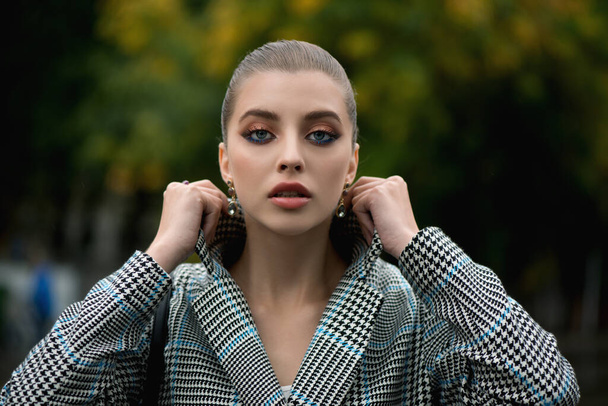 Beautiful stylish young woman in a coat walks along the street. Portrait of an attractive girl with professional color makeup. - Foto, afbeelding