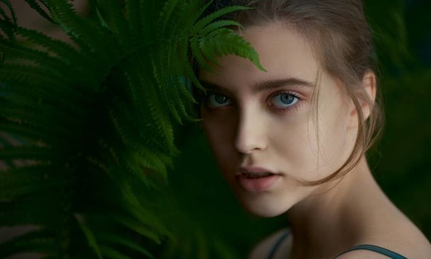 Beautiful young woman with perfect skin with tropical green fern leaf. SPA and wellness, body care and skincare concept.  Close up, selective focus. - Fotó, kép
