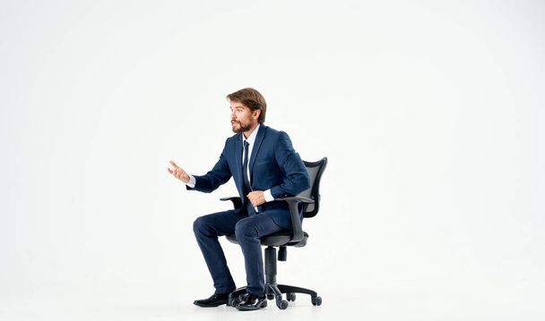 man met baard in een pak zitten in een kantoor stoel werk licht achtergrond - Foto, afbeelding