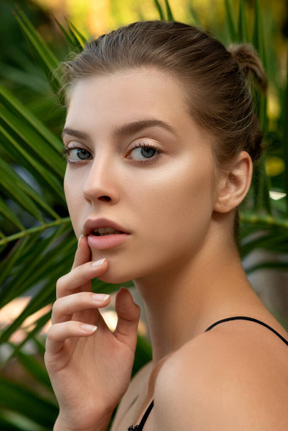 Beautiful young woman with clean perfect skin in tropical green leaves. Portrait of attractive model girl on ecological nature background. SPA and wellness, body care and skincare concept. - Φωτογραφία, εικόνα