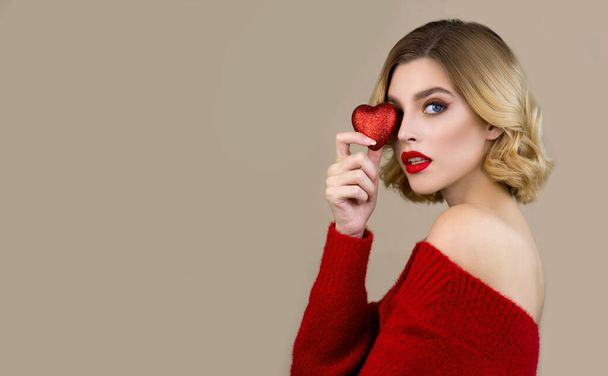 Beautiful young woman  with perfect young skin and professional makeup with red lips poses with red heart.  Skincare seasonal beauty concept. Christmas and New Year concept. Closeup, copy space. - Фото, зображення