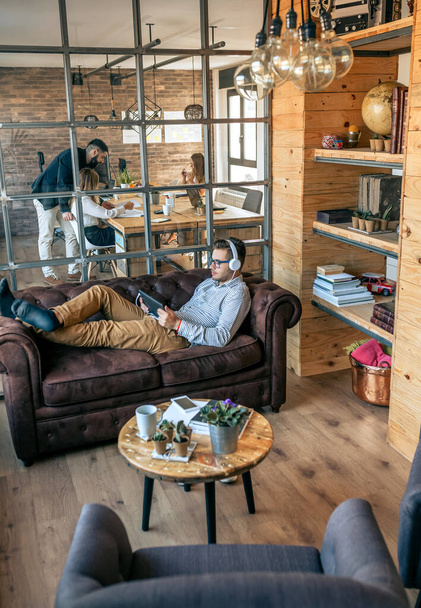 Επιχειρηματίας ξαπλωμένος σε καναπέ γραφείου με tablet - Φωτογραφία, εικόνα
