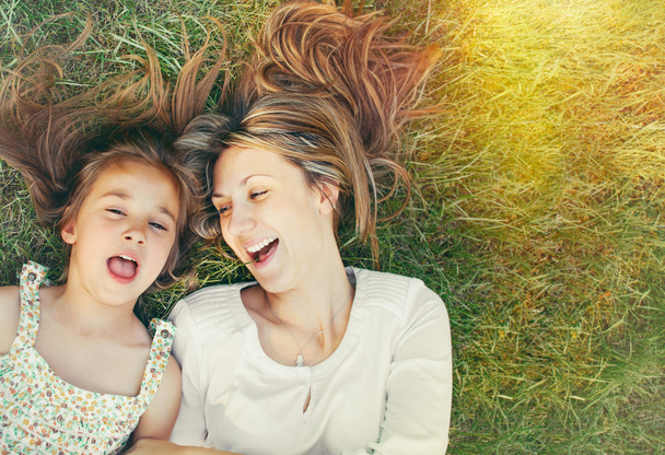 χαριτωμένο κοριτσάκι και η μητέρα της διασκεδάζοντας στο γρασίδι στην ηλιόλουστη - Φωτογραφία, εικόνα