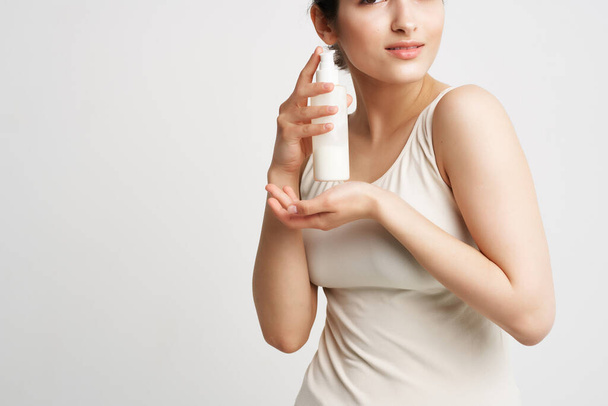 brunette in een witte tank top met lotion in haar handen schone huid - Foto, afbeelding