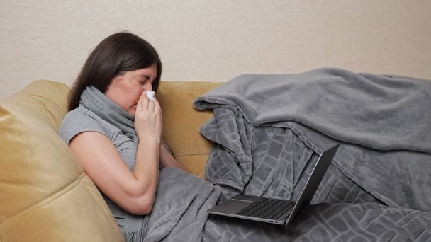 Woman freelancer coughs and types on laptop lying on sofa - Photo, Image