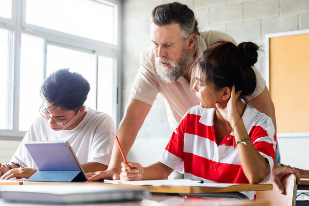 Caucasian mature adult man teacher with beard assisting teen high school students in class using tablet. Education concept. - Photo, Image