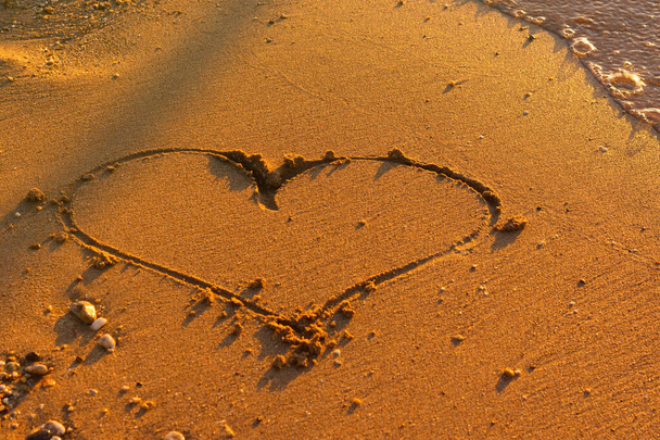 Corazón arena mar puesta de sol. Una romántica declaración de amor en la arena tropical naranja. Un símbolo solitario del corazón en la orilla del mar. El concepto de verano, relajación, descanso, sentimientos y creatividad. Copiar espacio - Foto, Imagen