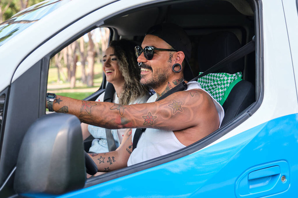 Молодая татуированная пара за рулем фургона и смеется. - Фото, изображение