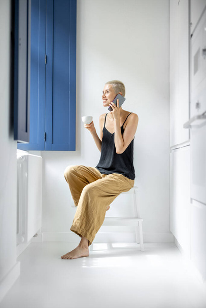 Femme avec téléphone et café près de la fenêtre à la maison - Photo, image